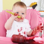 Naughty baby eating alone in the high chair